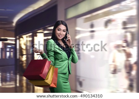 Shopping Asian woman talking on the phone and holding a paper bag looking behind