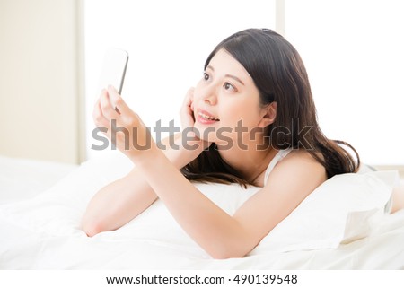 beautiful young asian woman taking selfie by smart phone on bed. girl bedroom background at home