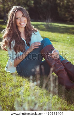 Beautiful woman is sitting on grass in autumn park