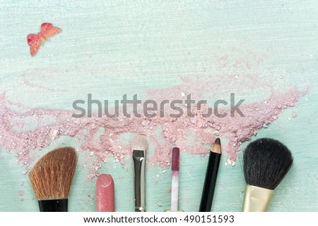 Makeup brushes and lipstick on a teal blue background, with traces of powder and blush  and watercolor butterfly. Horizontal template for makeup artist's business card or flyer design. With copyspace 