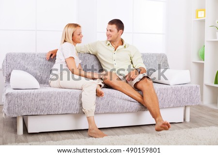 Beautiful young couple sitting on a sofa and looking at each other in the living room.