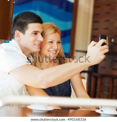Couple sitting in cafe and taking a picture with mobile phone.