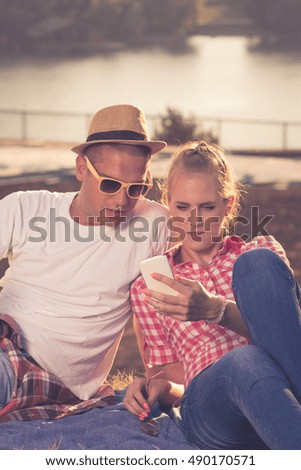 Beautiful young couple looking at the mobile smart phone together while sitting on the top of the hill