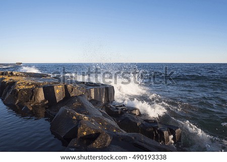 A landscape photo of small waves crashing into rocks on a blue lake.