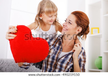 Little daughter giving her mother heart shaped pillow for mother's day. 