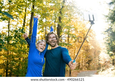 Beautiful runners in autumn forest taking selfie with smartphone