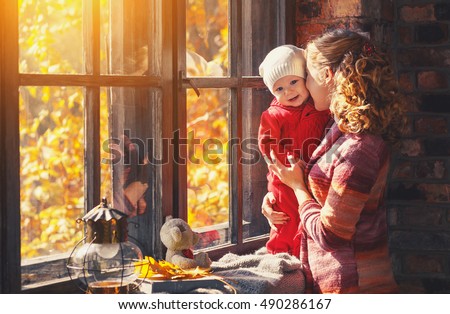 happy family mother and baby playing and laughing at the window in the fall