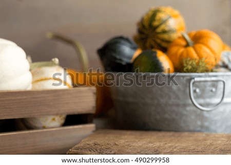 Shallow depth of field image showing pumpkins in a wooden crate and a steel bucket filled with gourds.  Focus on foreground, blurred background. Space for product or copy. 