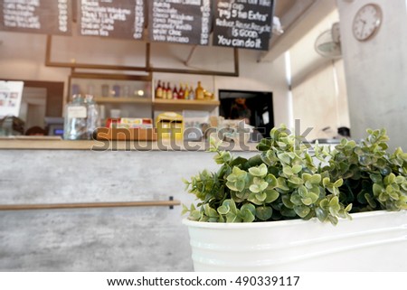 selective focus to green plastic plants in the white flower pot, defocussed to interior of coffee shop.