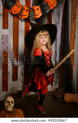 little cute halloween witch girl in costume and hat in red and black on broom, pumpkins and skull