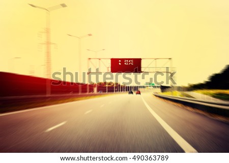 A Highway With Traffic on a Bright And Sunny Day. The Digital Temperature Indicator Shows the High Temperature on The Road. (Filtered image processed vintage effect and motion blur background.)