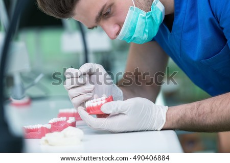 Dental prosthesis, dentures, prosthetics work. Prosthetics hands while working on the denture, false teeth, a study and a table with dental tools. Royalty-Free Stock Photo #490406884