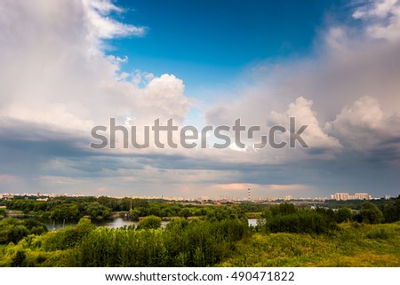 Beautiful natural landscape at sunset with green grass, flowers and cloudy sky. City building in distance. Image of recreation in countryside. Great outdoors picture.
