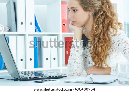 Female secretary with computer laptop working  in office looking at screen.
