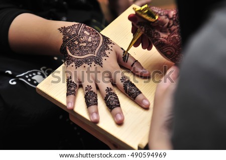 Artist applying henna tattoo on women hands. Royalty-Free Stock Photo #490594969