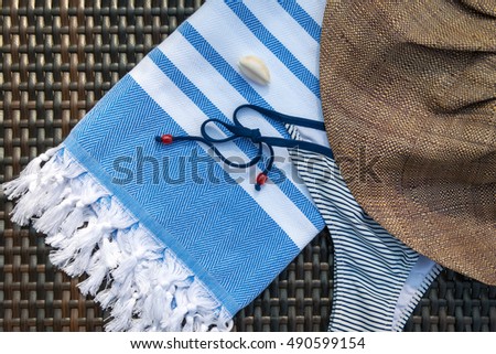 The concept of a flat lay summer accessories close-up of a white and blue Turkish peshtemal / towel, bikini, white seashells and straw hat on a rattan lounger.