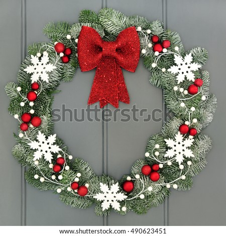 Christmas wreath with red baubles and bow and white snowflake decorations and snow covered blue spruce fir over grey front door background.