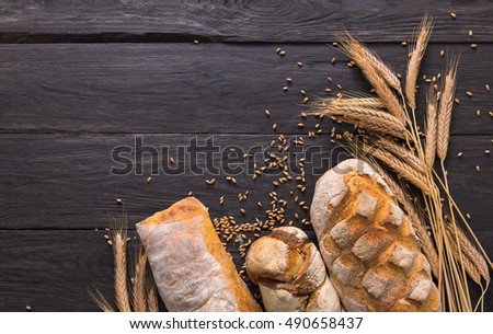 Bread border on wood with copy space background. Brown and white whole grain loaves still life composition with wheat ears scattered around. Bakery and grocery food store concept.