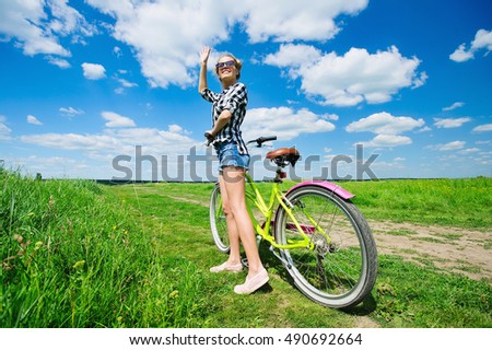 Beautiful girl pushing her bicycle outdoors across the green sunny field