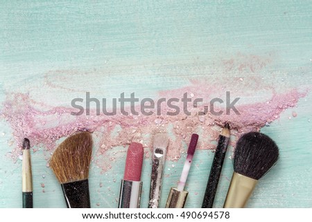 Makeup brushes and lipstick on a teal blue background, with traces of powder and blush on it. A horizontal template for a makeup artist's business card or flyer design. With plenty of copyspace