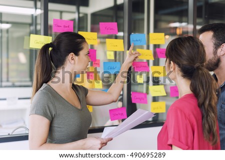 Three businesspeople discussing and planning concept. Front of glass wall marker and stickers. Startup office. Royalty-Free Stock Photo #490695289