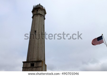 Lighthouse with american flag on cloudy sky background in Alcatraz