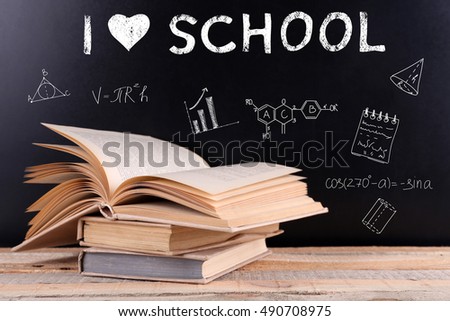Stack of books on wooden table. Text I LOVE SCHOOL and icons on blurred blackboard background. Knowledge concept.