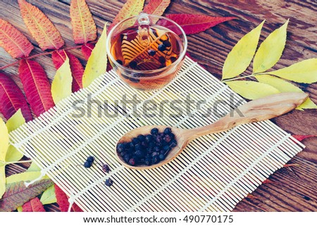 Drink From Dried Hawthorn Berries In Wooden Spoon On The Table With Colorful Autumn Leaves. Top View Closeup. Tinted image. Autumn concept