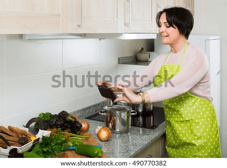 Brunette spanish  housewife in apron taking photo of dinner indoors