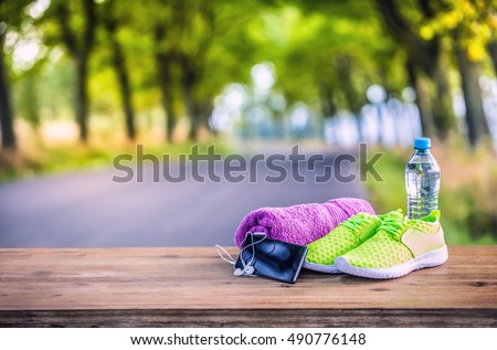 Pair of yellow green sport shoes towel water smart pone and headphones on wooden board. In the background forest or park trail. Accessories for running sport.