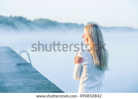 Woman warming at a first sun rays in the morning in the peaceful place at the lake after practicing yoga. Above the lake is a mist.