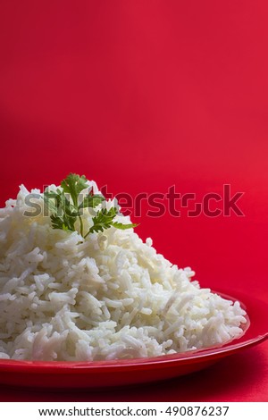 Cooked plain white basmati rice with corriander in a red plate on red background