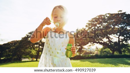 Adorable cute young girl blowing bubbles playing outside