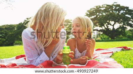 Mother and daughter relaxing together blowing bubbles in the park