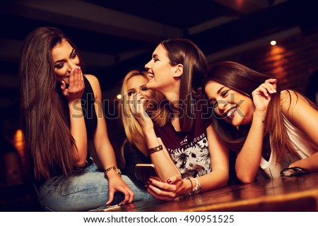 group of young women friends having fun looking at something funny on their smart phone and laughing Royalty-Free Stock Photo #490951525