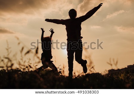 father and son jumping at sunset sky