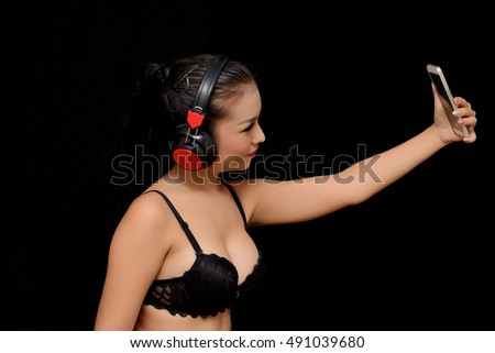 Pretty girl take a self portrait with her smart phone. Asian girl selfie,
 low key portrait over dark background

