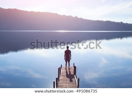 dreamer, silhouette of man standing on the lake wooden pier at sunset, human strength, psychology concept Royalty-Free Stock Photo #491086735