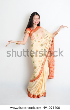 Portrait of young mixed race Indian Chinese woman in traditional sari dress dancing, on plain background.