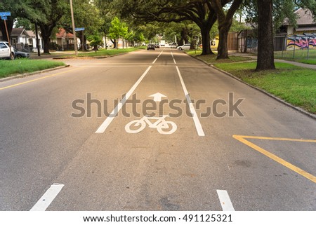 White bicycle sign on asphalt bike lane on city street with cars in background. Concept background for Air Pollution Reduce and Cycling Health Benefits.