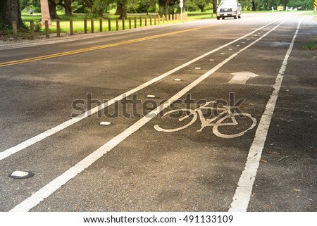 White bicycle sign on asphalt bike lane on city park with car in background. Concept background for Air Pollution Reduce and Cycling Health Benefits.