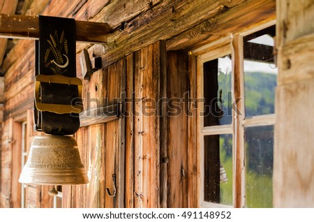 Rustic alpine cow bell hanging at old farm hut, mountains reflection on windows. Sign in German "1987 Fritz Knutti. Birthday of yours" on a bell. Photo taken in Adelboden, Switzerland