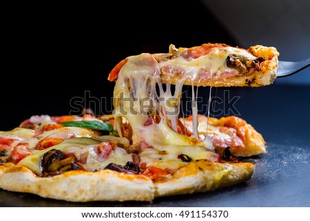 cut off a slice of pizza. melted cheese stretches from the piece Royalty-Free Stock Photo #491154370