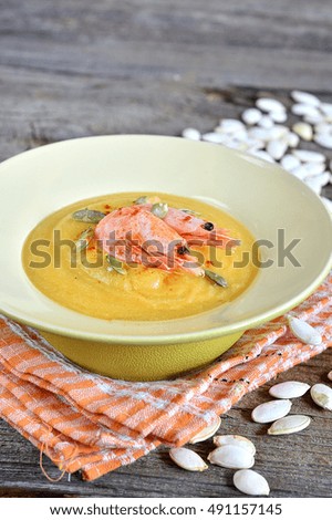 Pumpkin puree soup with shrimps and sunflower seeds on a wooden background