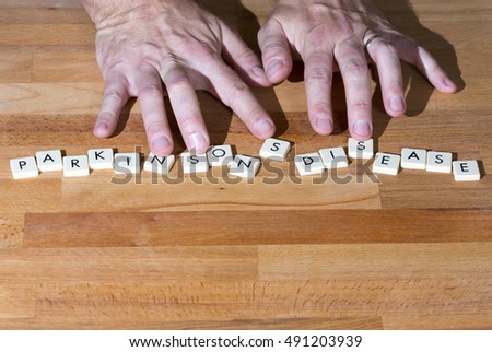 Parkinson's disease text on a wooden table. Shaking fingers touches the letters. Royalty-Free Stock Photo #491203939