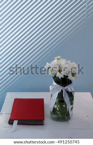 Bouquet of chrysanthemums and red book on a background of shadows from the blinds