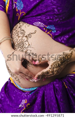 A color photo of a henna tatoo on a woman's pregnant belly and hands in shape of heart.