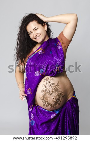 studio portrait of a happy pregnant woman in Indian sari, a pregnant belly painted with henna
