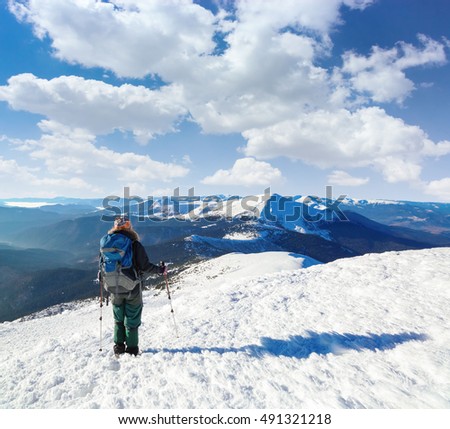 Majestic winter scenery. The tourist is going to the goal through the snowy lawn and before the view there are unbelievable beautiful mountains covered with snow and blue sky.