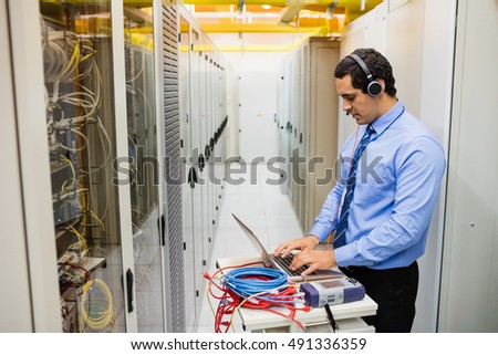 Technician in head phones using laptop in server room